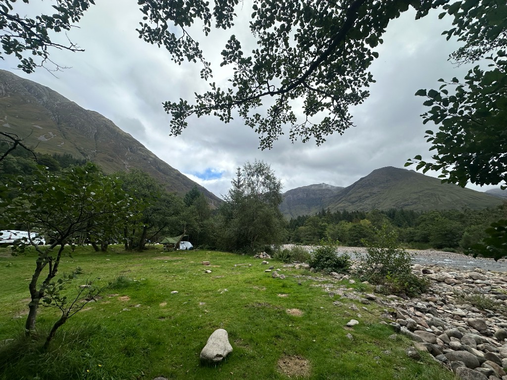 Daytime pitch at Red Squirrel: grass, trees, a small tent, and the river running into Glen Coe