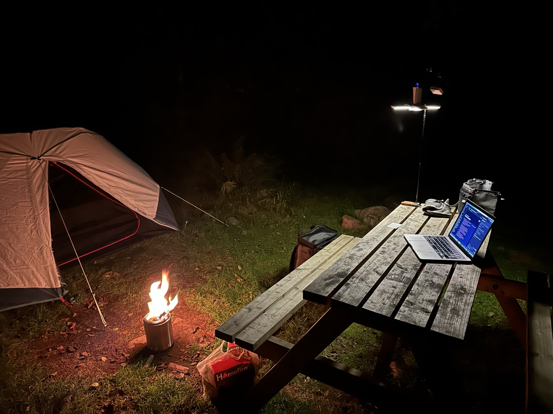 Picnic table, lamp and laptop beside the tent and stove at Red Squirrel