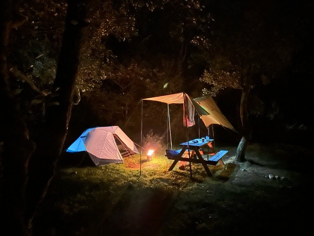 Night pitch at Red Squirrel: two-man tent, stove, and a picnic table under a tarp in the woods