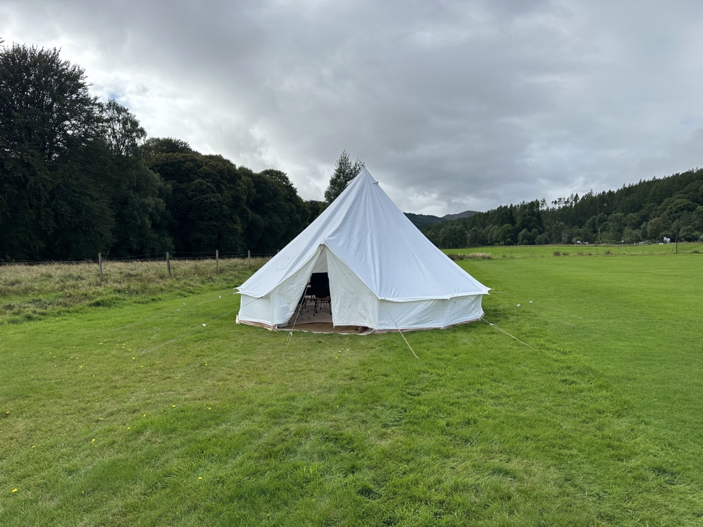 6M bell tent on the event field with the door open under a grey Highland sky
